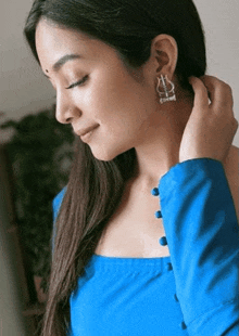 a woman wearing a blue shirt and earrings is adjusting her earring .