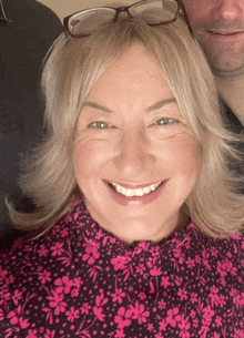 a woman wearing glasses and a pink floral shirt is smiling