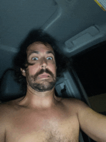 a shirtless man with a beard is taking a selfie in a car