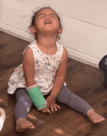 a little girl with a green cast on her arm is sitting on the floor crying