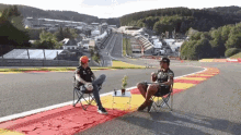 two men sit in chairs on a race track with one wearing a shirt that says ' gm ' on it