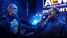 a man holding a microphone in front of a sign that says aew