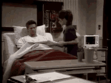 a man is laying in a hospital bed while a nurse talks to him .