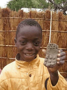 a young boy in a yellow jacket is holding a piece of clay in his hand