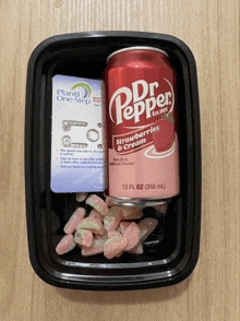 a can of dr pepper sits in a plastic container with gummy bears