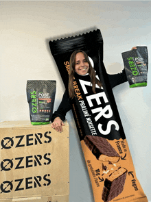 a woman holds up a zeros protein bar next to a bag of post workout