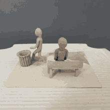 a clay sculpture of two people sitting on a bench and a trash can