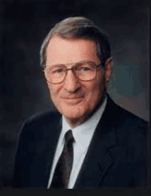 a man in a suit and tie is wearing glasses and smiling for the camera .