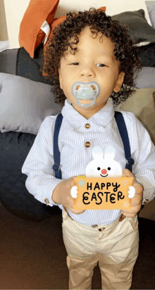 a young boy with a pacifier in his mouth is holding a happy easter sign