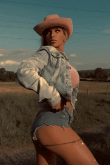 a woman wearing a cowboy hat and denim shorts stands in a field