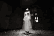 a ghostly woman in a white dress is standing in a dark room in front of a window .