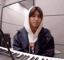 a young man in a hoodie is sitting at a piano .