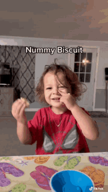 a young boy in a red shirt is sitting at a table with a bowl of food and eating a mummy biscuit