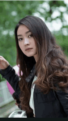 a woman with long hair is wearing a black jacket and holding a pink balloon .