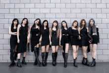 a group of women standing in front of a brick wall wearing all black