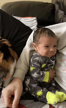 a baby wearing a dinosaur pajama is laying on a bed next to a cat