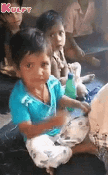 a group of children are sitting on the floor and one of them is holding a bottle of water .