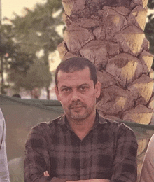 a man in a plaid shirt stands with his arms crossed