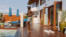 a man without a shirt is dancing on a wooden deck next to a swimming pool