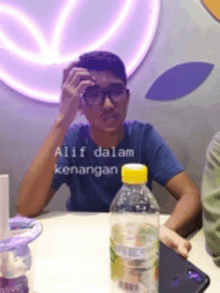 a young man wearing glasses sits at a table with a bottle of evian water in front of him