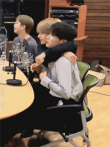 three men are hugging each other while sitting at a table in front of microphones