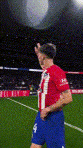 a man in a red and white striped shirt and blue shorts is standing on a soccer field with his hand up .