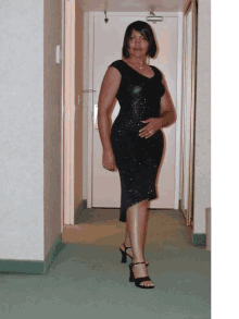 a woman wearing a black dress and heels stands in a hallway