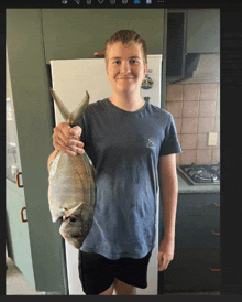 a young man holding a fish in front of a fridge