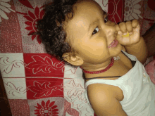 a little girl with curly hair is laying on a red and white floral blanket