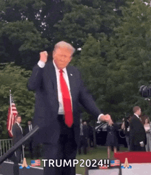 a man in a suit and tie is dancing in front of a crowd and a sign that says trump2024