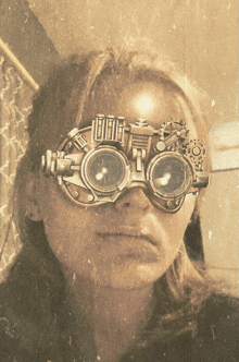 a woman wearing a pair of steampunk goggles looks at herself in the mirror