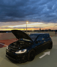 a black car with the hood up is parked in a parking lot