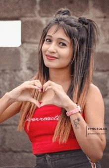 a young woman in a red top is making a heart shape with her hands .