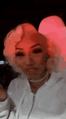 a woman with blonde hair and a pearl necklace is taking a selfie with a red light behind her .