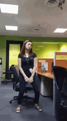 a woman in a black shirt is dancing in an office with a yellow cubicle that says " all stakeholders " on it