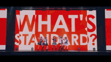 a group of girls are dancing on a stage in front of a large red and white sign that says what 's standard