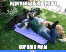 a man laying on a blanket in the grass with a computer and headphones on