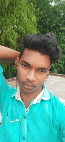 a young man wearing ear buds and a green shirt takes a selfie