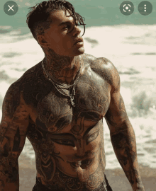 a man with a lot of tattoos on his body stands on the beach