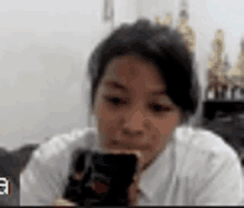 a woman in a white shirt is holding a cell phone in front of her face .