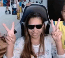 a woman wearing sunglasses is sitting in a chair making a peace sign .