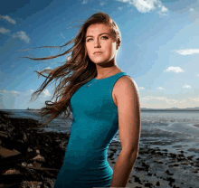 a woman in a blue dress is standing on a beach