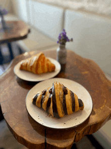 two croissants are on a wooden table with a vase of purple flowers in the background