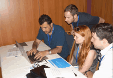 a group of people looking at a laptop with one man wearing a lanyard that says ' european union ' on it