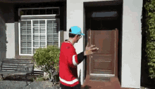 a man in a red and white jersey and a blue hat is standing in front of a house .