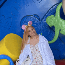 a woman wearing pink mickey mouse ears stands in front of a blue wall that says bark