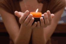 a woman is holding a small orange candle in her hands