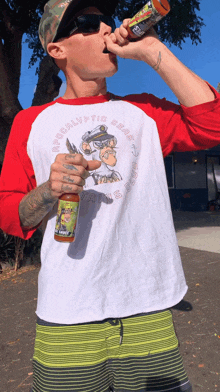 a man wearing a red and white shirt with the word apocalypse on it is drinking from a can