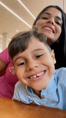 a woman in a pink shirt that says ' abercrombie & fitch ' on it smiles next to a young boy