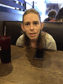 a woman sits at a table with a phone and a glass that says coca cola